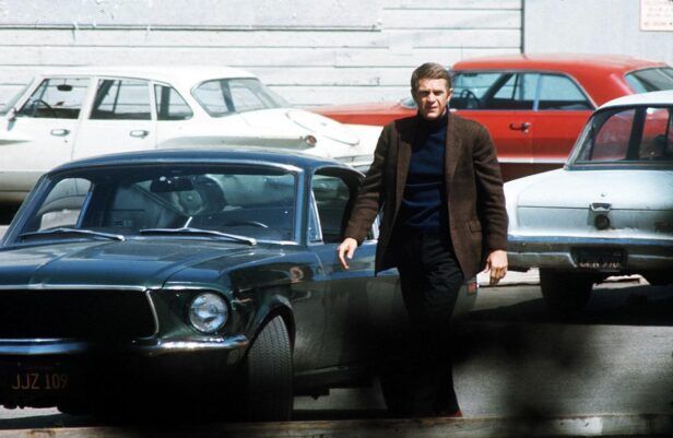 Brown tweed sport coat with navy turtleneck and dark trousers, worn beside a green fastback in a styled scene