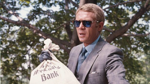 Grey three-piece suit with light blue shirt, blue tie and white pocket square, worn in a film scene
