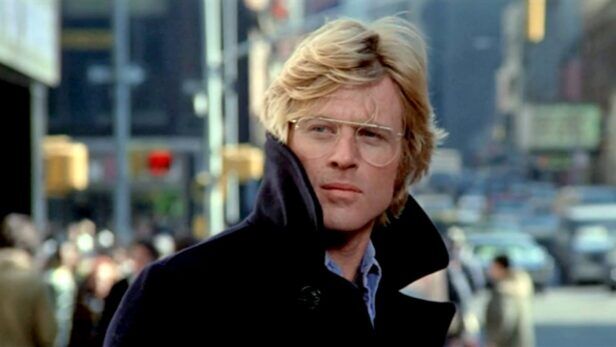 Navy wool duffle coat with popped collar over a blue chambray shirt, worn on a city street in a film still