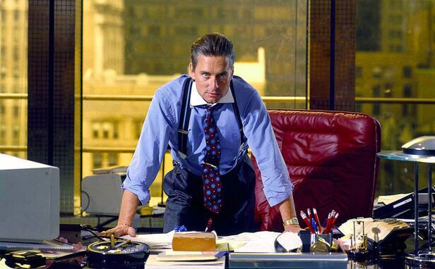Blue contrast-collar dress shirt with burgundy medallion tie and braces, worn at an office desk in a film still