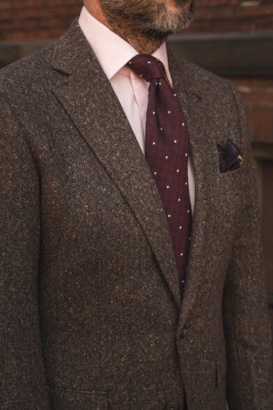 Burgundy silk necktie with white dots, worn with a pink shirt and brown donegal tweed jacket, a close-up detail