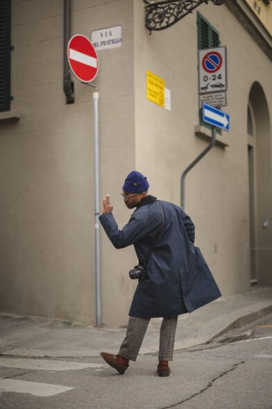 Navy cotton raglan trench coat with houndstooth trousers, brown suede loafers and blue beanie, worn on a city street