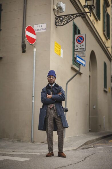 Navy field coat over a brown checked wool suit with medallion tie, beanie and suede loafers, on a city street