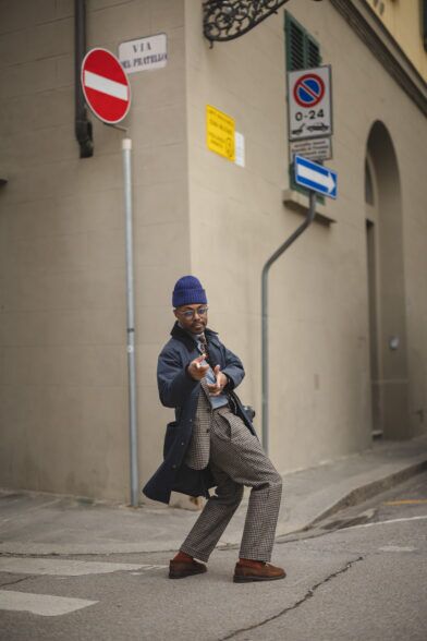 Navy raincoat over a houndstooth check suit with blue beanie and brown suede loafers, styled on a street corner
