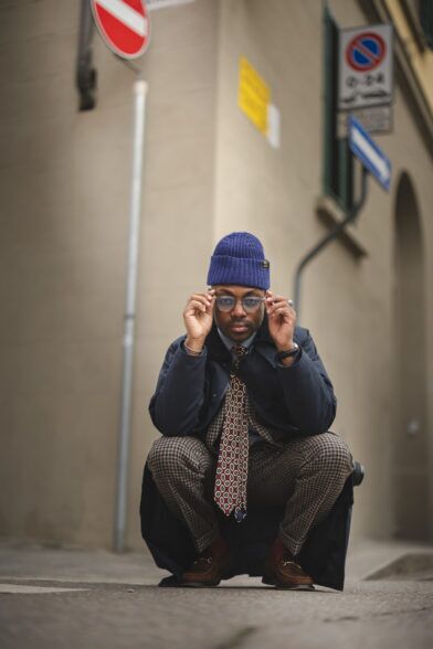 Burgundy medallion silk necktie with navy overcoat, checked trousers and blue beanie, worn by a model on a street