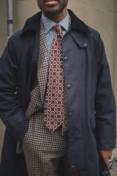 Burgundy paisley silk necktie with chambray shirt, brown check tweed jacket and navy corduroy-collar coat, worn by a model