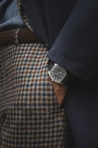 Brown and green houndstooth wool trousers with woven leather belt, navy jacket and field watch, a styled detail