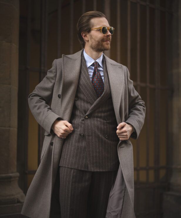 Brown chalk stripe double-breasted flannel suit with taupe overcoat, striped shirt and red medallion tie, worn by a model