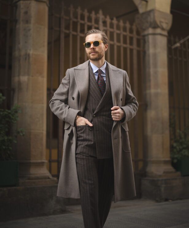 Taupe wool overcoat over a brown chalk stripe double-breasted suit with medallion tie, on a street