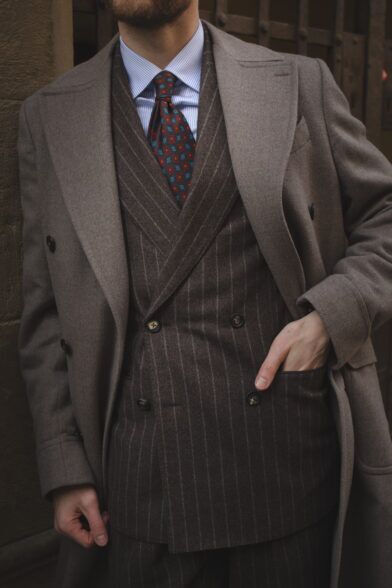 Brown chalkstripe flannel double-breasted suit with taupe overcoat, striped shirt and red medallion tie, worn by a model