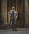 Brown chalk stripe double-breasted suit with taupe wool overcoat and patterned tie, worn on a street
