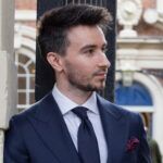 Navy peak lapel suit with white shirt, navy grenadine tie and burgundy dotted pocket square, worn by a model