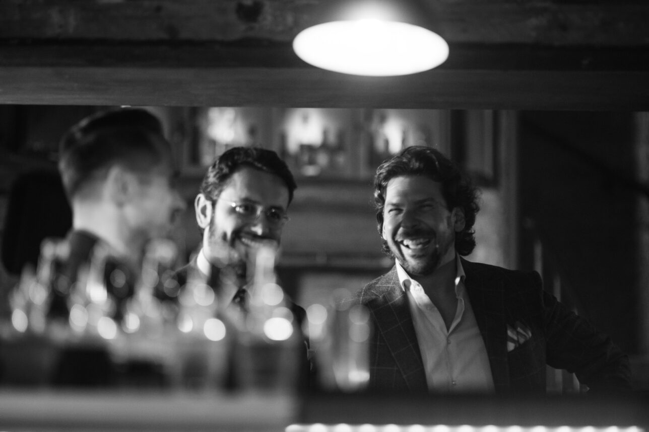 Windowpane check sport coat with open white shirt and pocket square, worn at a bar in a black and white lifestyle scene