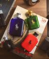 Men's fragrance bottles in blue, green, red, amber and black arranged with books on a wood desk, styled flat lay