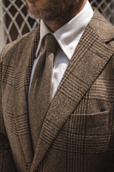 Textured brown wool necktie with white polo shirt and brown glen check tweed jacket, a close-up detail