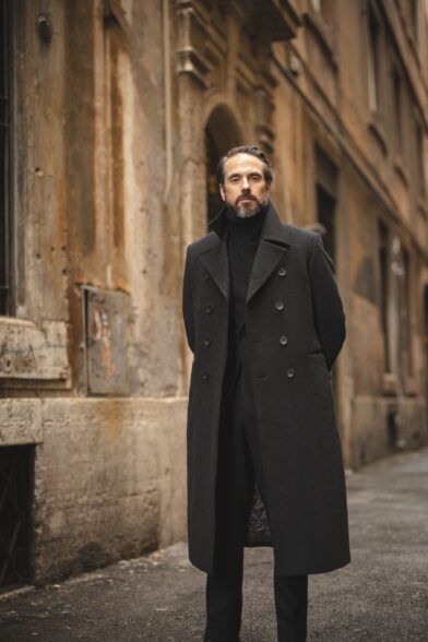 Charcoal double-breasted wool overcoat with black turtleneck and black trousers, worn by a model on a city street