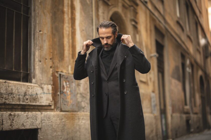 Charcoal double-breasted wool overcoat over a black suit and turtleneck, worn by a model on a street