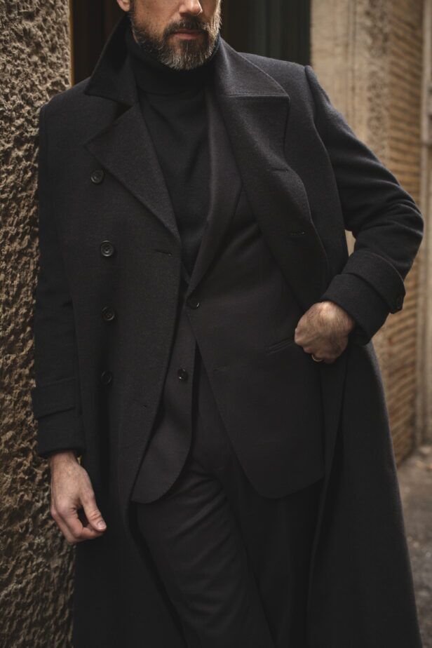 Black wool double-breasted overcoat layered over a black suit and turtleneck, worn by a model on a street
