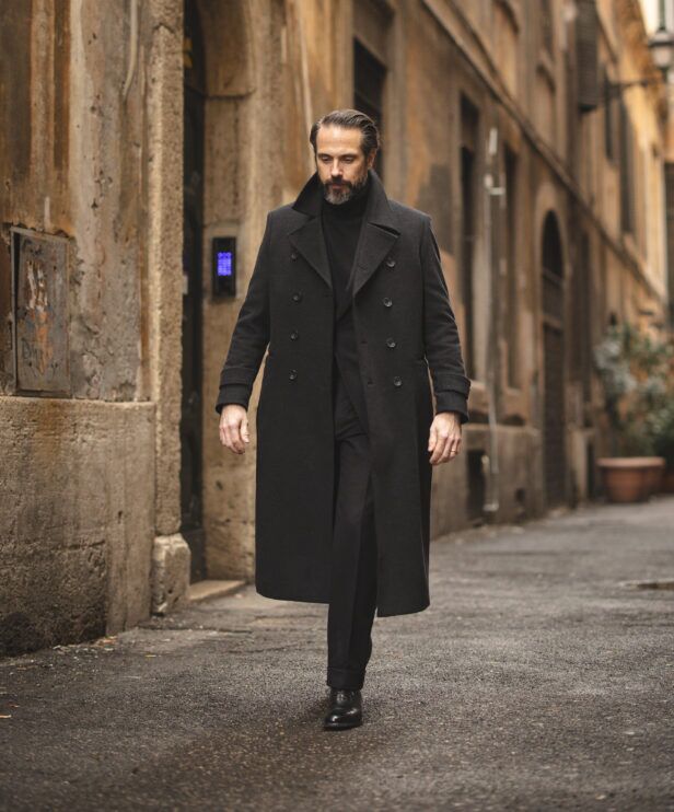 Charcoal double-breasted wool overcoat with black turtleneck, trousers and derbies, worn by a model on a cobbled street
