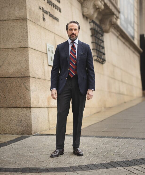 Navy blazer with gold buttons, burgundy striped tie and charcoal trousers, worn on a city street