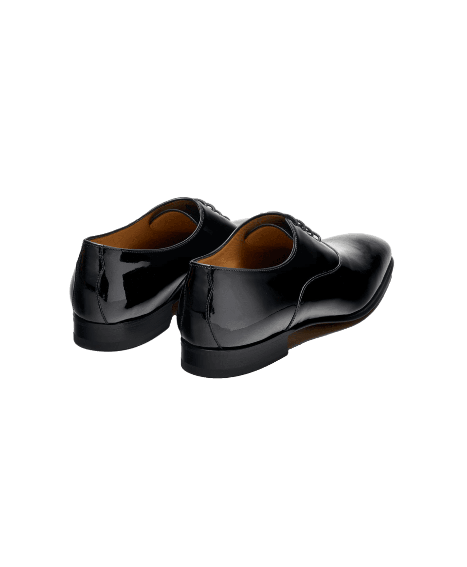 Black patent leather oxford shoes with leather soles, back view on black background