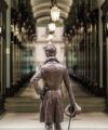 Bronze statue of Beau Brummell in frock coat with top hat and cane, facing a lamp-lit London shopping arcade, lifestyle scene