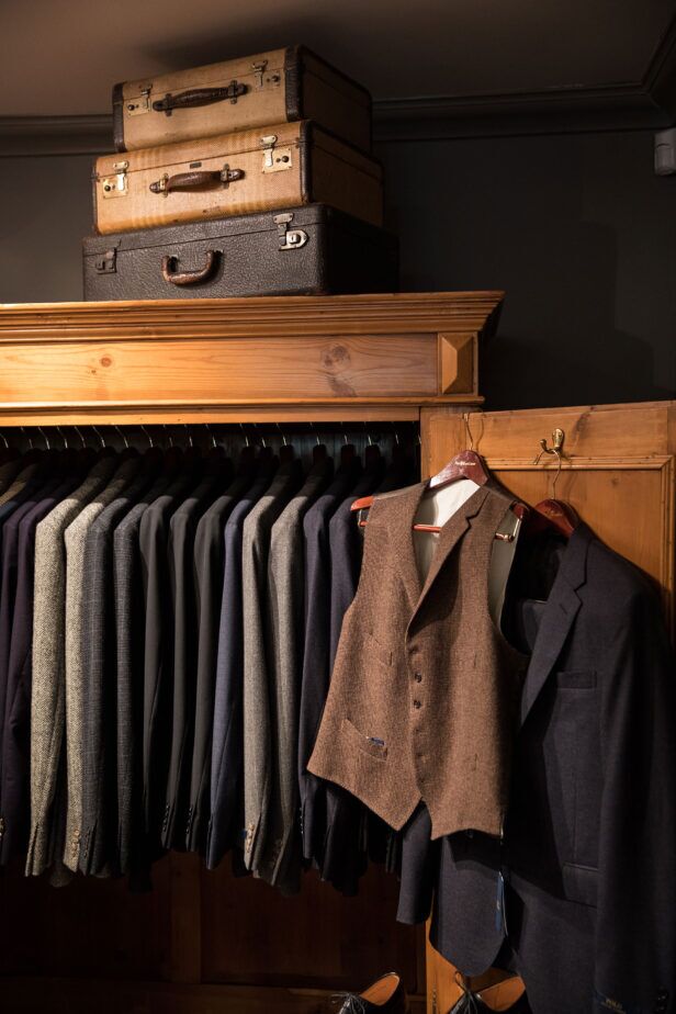 Brown houndstooth wool waistcoat on a hanger beside a rail of tweed and flannel jackets in a tailoring shop