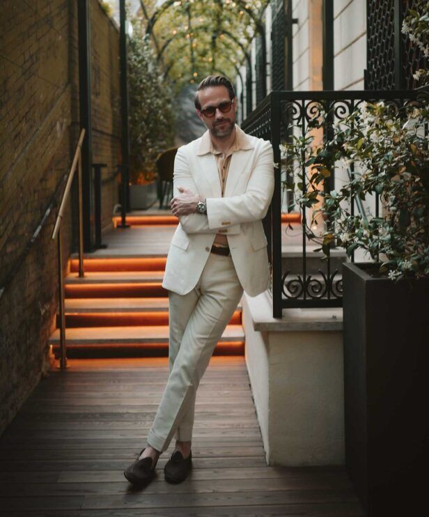 Cream two-piece suit with tan camp collar shirt and brown loafers, worn by a model on a lit garden stairway