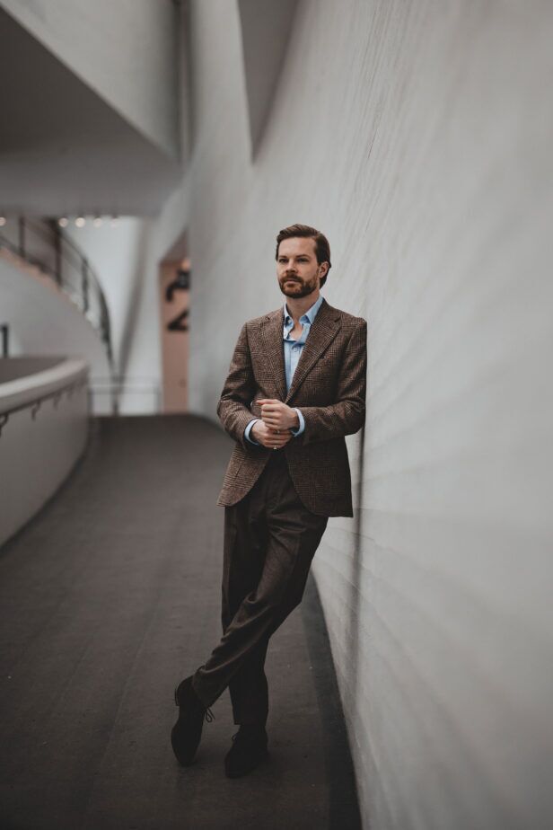 Brown checked wool sport coat with light blue shirt, brown flannel trousers and dark suede shoes, worn by a model
