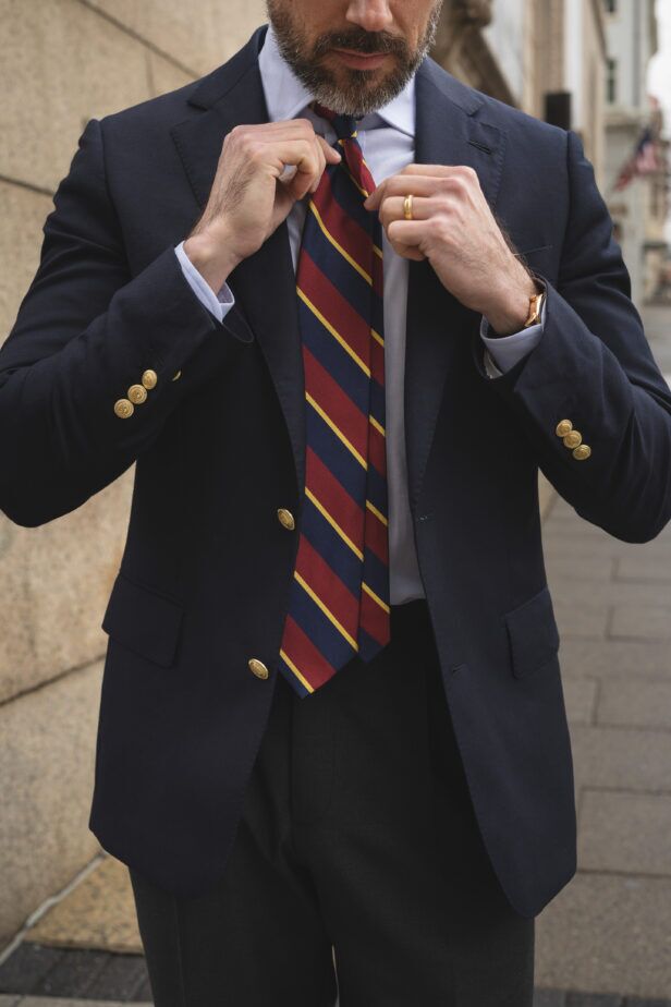 Navy blazer with gold buttons, burgundy and navy repp stripe tie and white shirt, worn by a model on the street