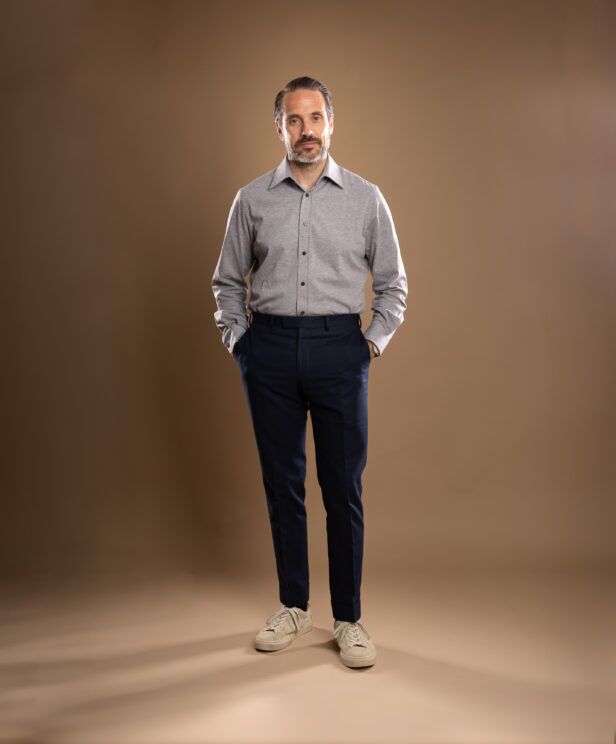 Grey knit cotton dress shirt with navy cuffed trousers and off-white sneakers, worn by a model