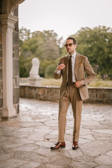 Tan solaro suit with white shirt, brown knit tie and brown double monk shoes, worn by a model on a stone terrace