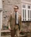 Tan solaro two-button suit with white shirt, brown knit tie and gold pocket square, worn by a model outdoors