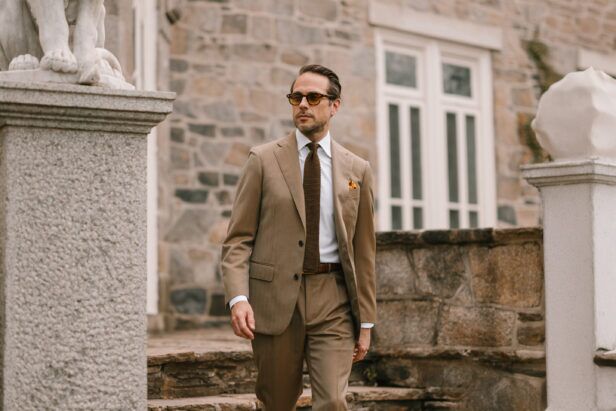 Tan solaro two-button suit with white shirt, brown knit tie and gold pocket square, worn by a model outdoors