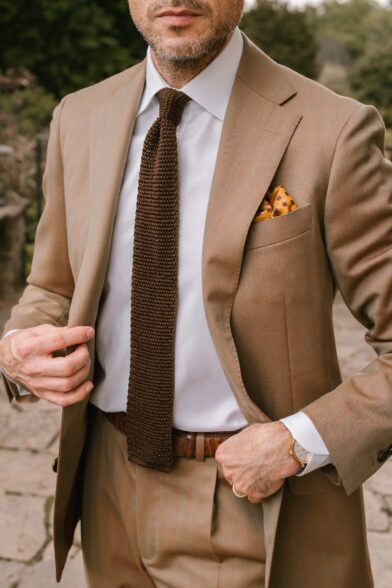 Tan solaro suit with white shirt, brown silk knit tie and gold patterned pocket square, worn by a model