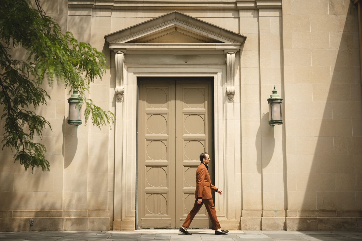 Terracotta hopsack suit with black turtleneck and loafers, worn by a model walking past a stone doorway