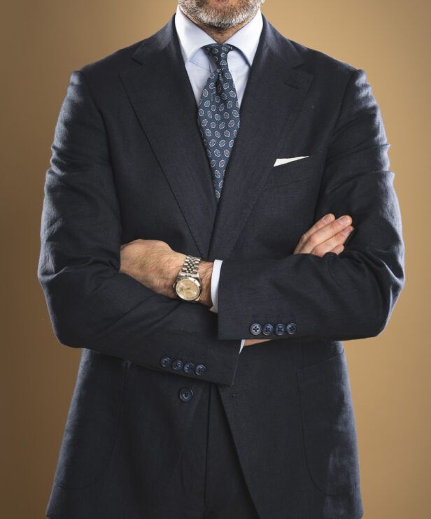 Navy linen sport coat with blue medallion silk necktie, light blue shirt and white pocket square, worn by a model
