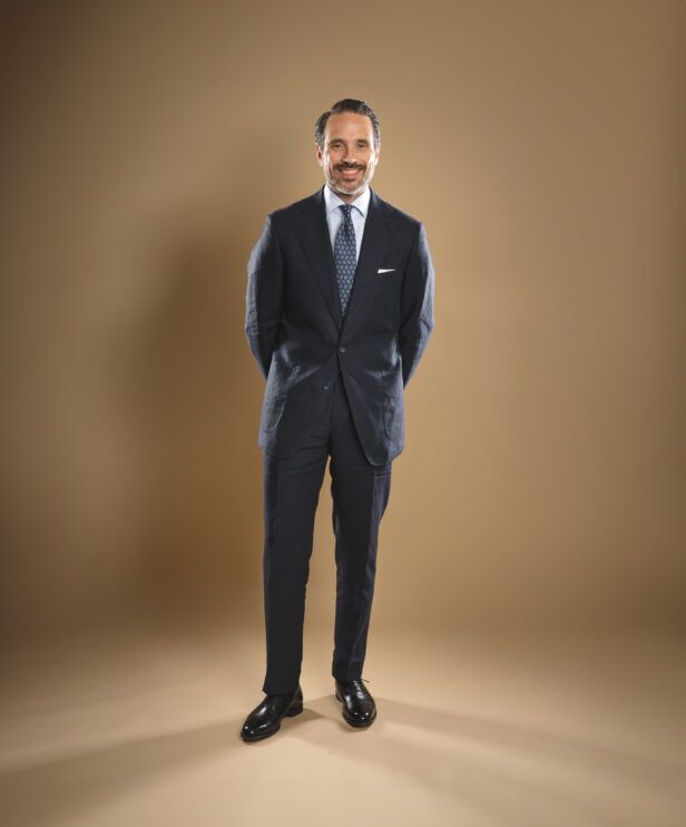 Navy linen two-button suit with white shirt, blue medallion tie and white pocket square, worn by a model