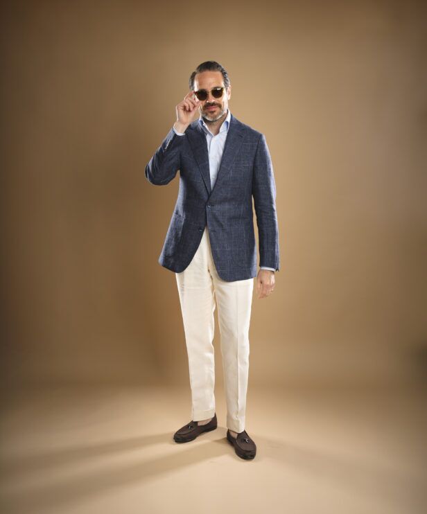 Blue checked linen sport coat with light blue shirt, cream trousers and brown tassel loafers, worn by a model