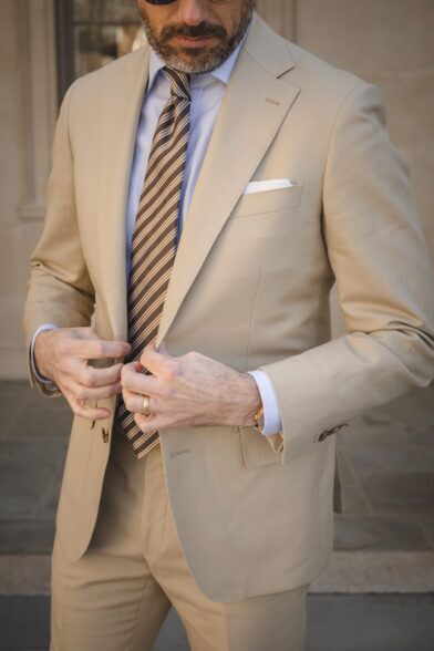Khaki cotton suit with light blue shirt, brown striped tie and white pocket square, worn by a model
