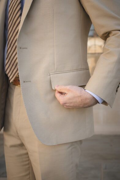 Khaki cotton suit jacket with flap pocket and brown striped tie, a close-up detail on a model