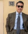 Olive brown wool suit with blue striped shirt and navy elephant-print silk tie, worn by a model on a street