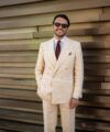 Cream double-breasted linen suit with peak lapels, white shirt and burgundy medallion tie, worn by a model