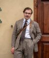 Taupe glen check suit with white shirt, brown medallion tie and a tan leather bag strap, worn on the street