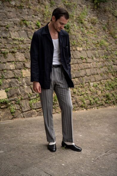 Navy chore jacket with white tank, grey chalk stripe wide-leg trousers and black loafers, worn by a model in a street scene