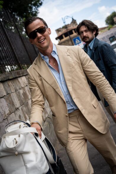 Tan cotton suit with light blue striped shirt and white holdall, worn on a street in a styled lifestyle scene