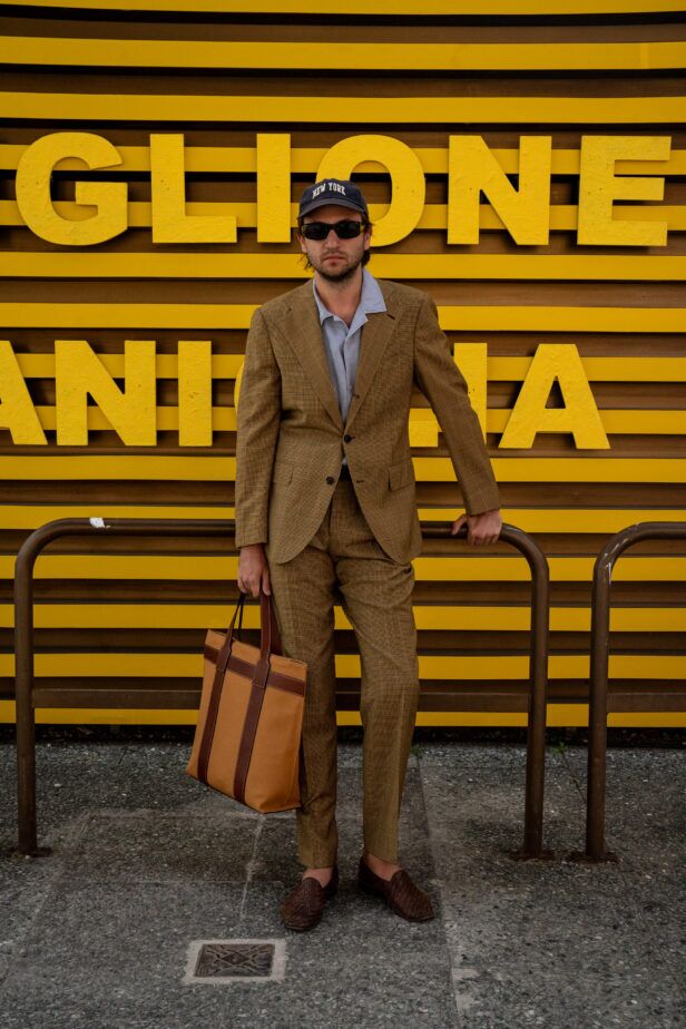 Tan checked suit with pale blue open-collar shirt, tan tote and woven loafers, worn by a man on the street