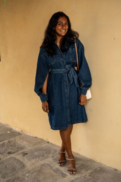 Indigo denim shirt dress with belted waist and split sleeves, styled with tan bag and heeled sandals, worn by a model