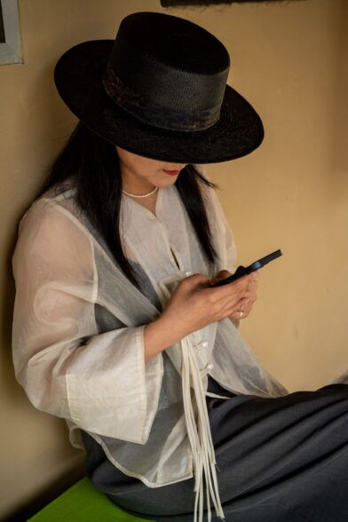 Black woven straw hat with patterned band, worn with a sheer ivory jacket and grey trousers in a street scene