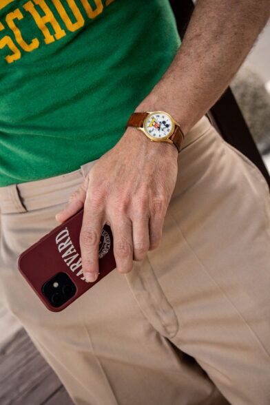 Gold-cased Mickey Mouse watch on brown leather strap with green tee and khaki trousers, a close-up detail